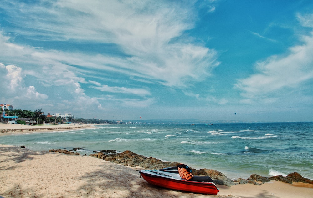 red kayak on brown sand near body of water during daytime