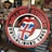 A circular logo featuring red lips with a tongue displaying the Union Jack flag in the center. The text 'Rolling Stones' arches over the top and 'Established 1962' curves along the bottom. The background showcases various merchandise and colorful items including comic book art and signs, one of which contains a Superman logo.