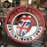 A circular logo featuring red lips with a tongue displaying the Union Jack flag in the center. The text 'Rolling Stones' arches over the top and 'Established 1962' curves along the bottom. The background showcases various merchandise and colorful items including comic book art and signs, one of which contains a Superman logo.