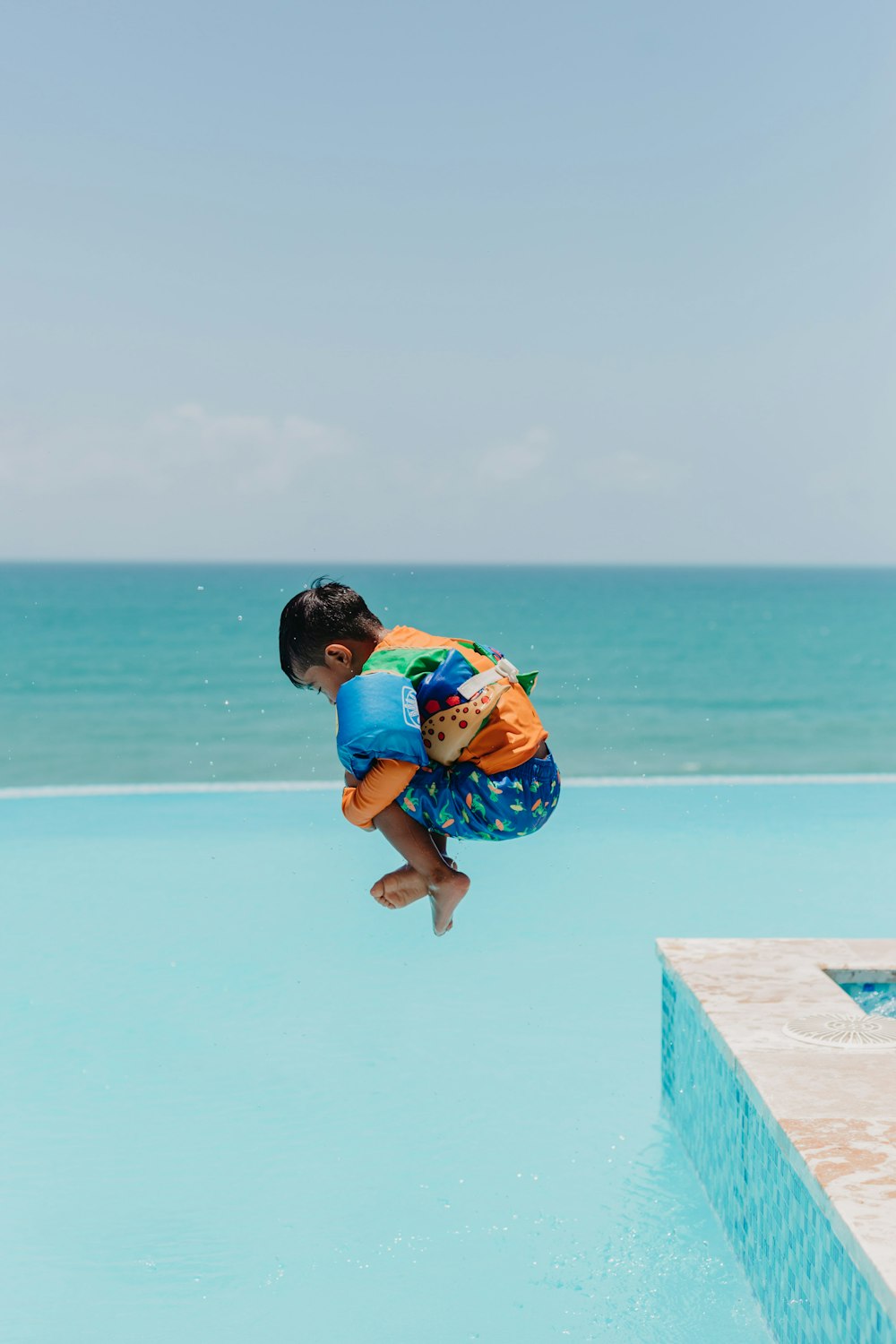 boy in blue and yellow t-shirt and blue shorts jumping on concrete dock during daytime