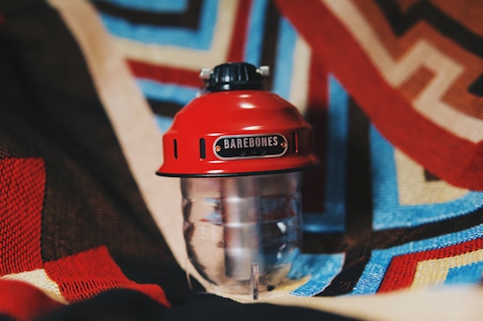 A red lantern with the brand name 'Barebones' displayed on it rests against a colorful, patterned textile background.