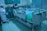 A modern hospital room featuring an adjustable hospital bed with side rails, a blue sheet, and medical devices such as monitors and an infusion pump nearby. The room is tiled, with a curtain in the background and medical equipment along the walls.