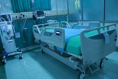 A sleek, motorized ICU bed with Trendelenburg and safety-lock features in a bright hospital room.