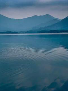 A serene Erhai lake view at dawn with mist gently rolling over the water and mountains.