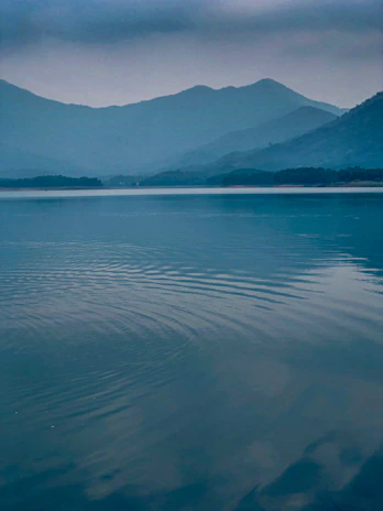 A serene Erhai lake view at dawn with mist gently rolling over the water and mountains.