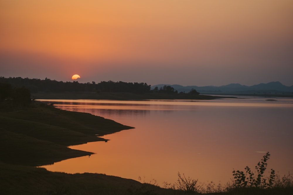 body of water near trees during sunset