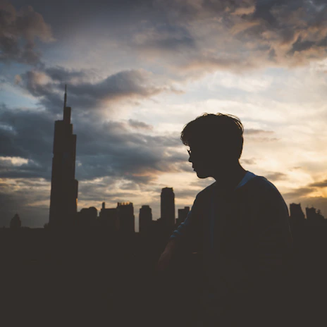 Traveler with suitcase looking at a vibrant city skyline during sunset.