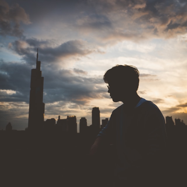 A smiling person holding a credit card with a city skyline in the background at sunset.