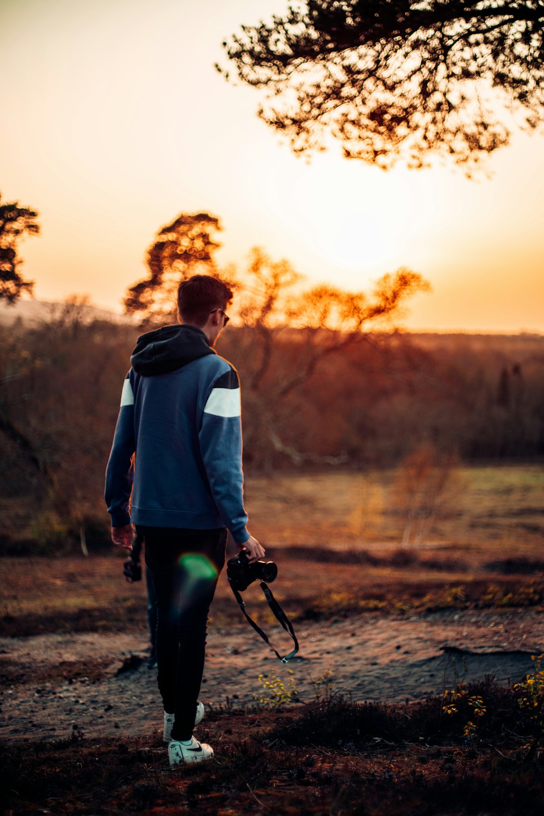 man in blue hoodie and black pants walking on dirt road during daytime