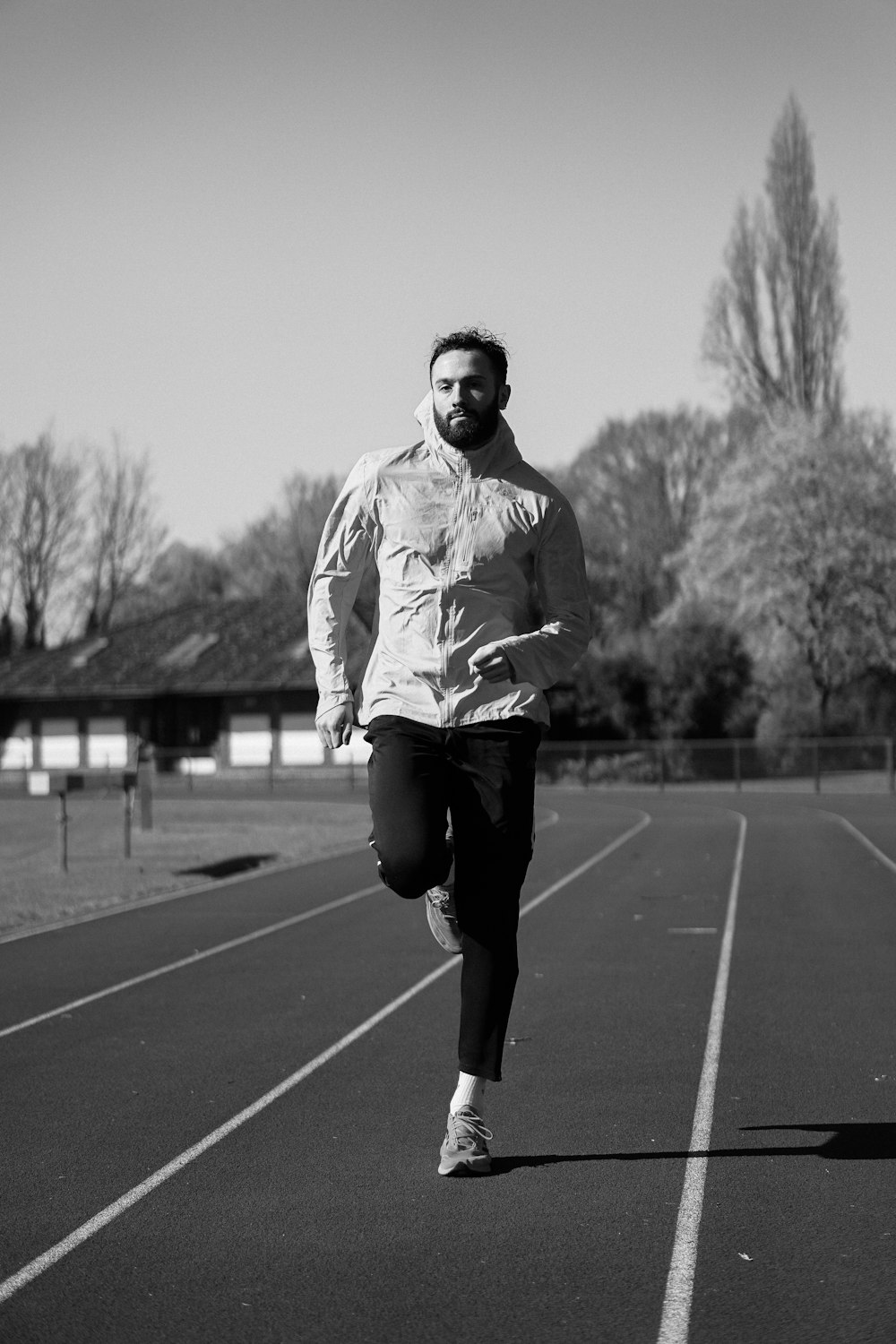 man in white and black hoodie running on track field in grayscale photography