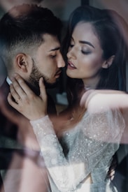 A close-up of a romantic and intimate moment between a couple, with soft lighting and a dreamy atmosphere. The woman is wearing a detailed, lace-patterned garment.