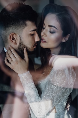 A close-up of a romantic and intimate moment between a couple, with soft lighting and a dreamy atmosphere. The woman is wearing a detailed, lace-patterned garment.