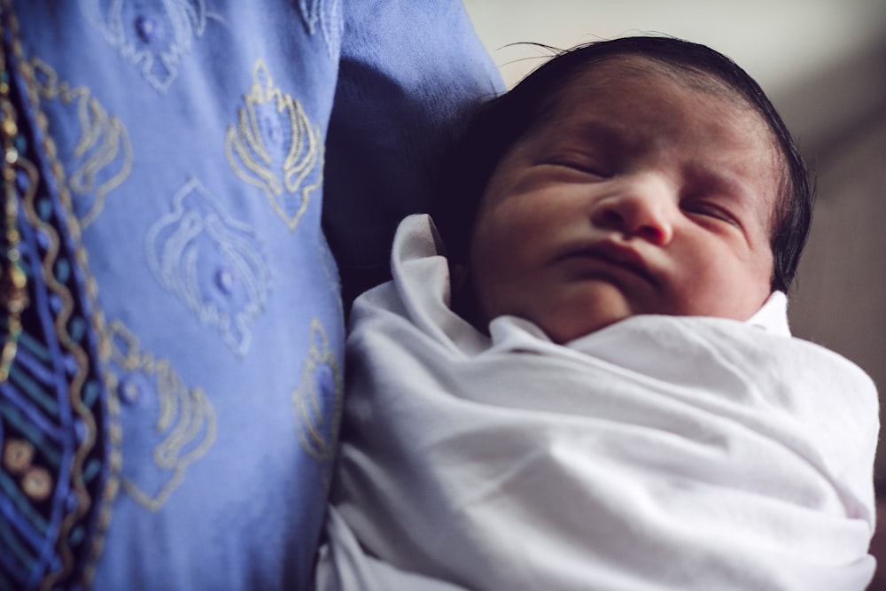 baby in white shirt lying on blue textile