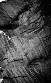 Abstract patterns formed by the natural striations and textures of a rock surface, showcasing intricate layers and grooves. The image is in black and white, highlighting the contrast and details in the rock formations.