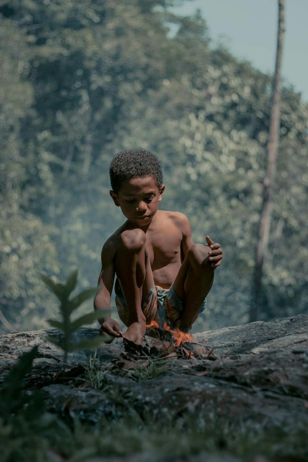 topless man in blue and red shorts sitting on rock