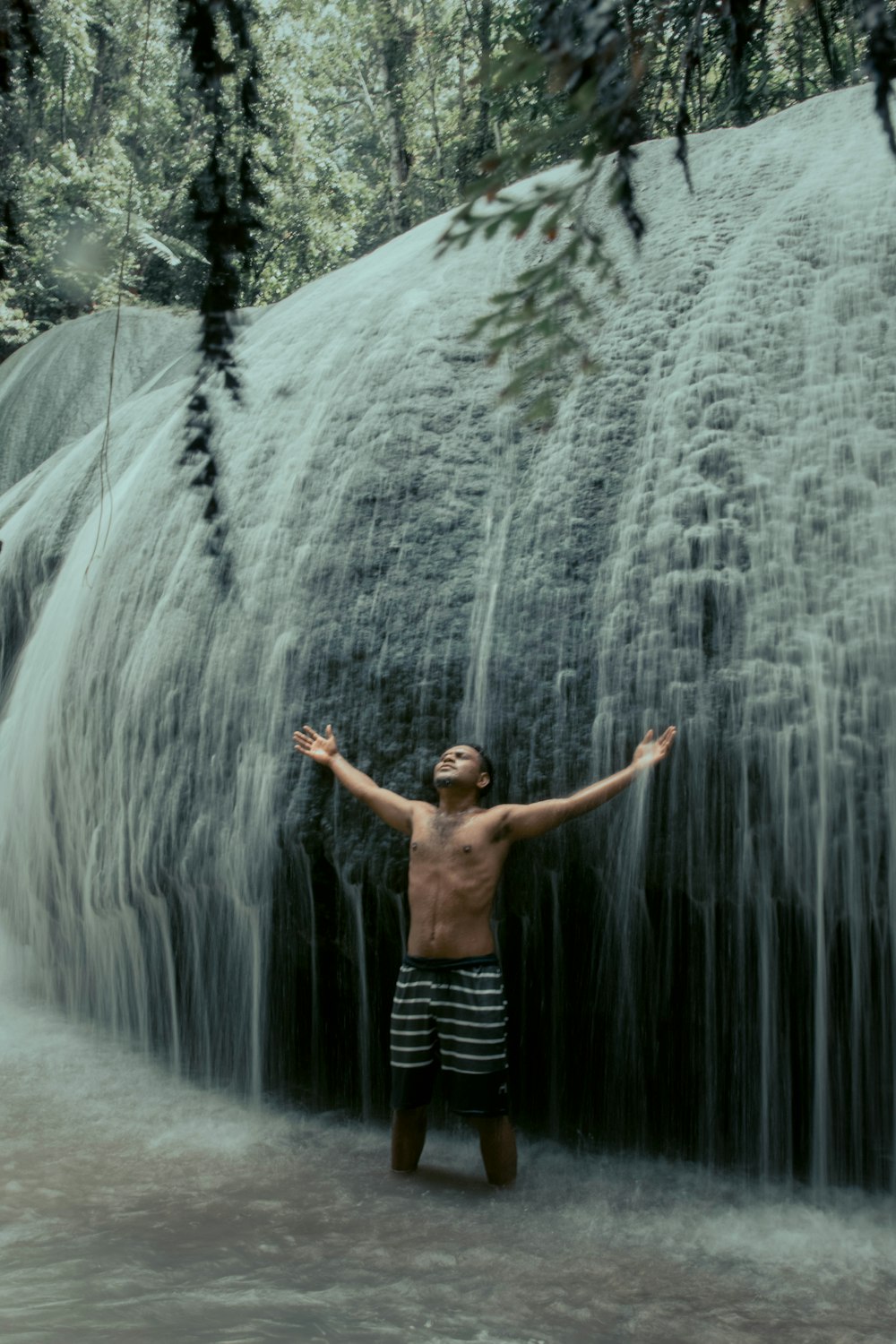 man in black shorts standing in front of waterfalls