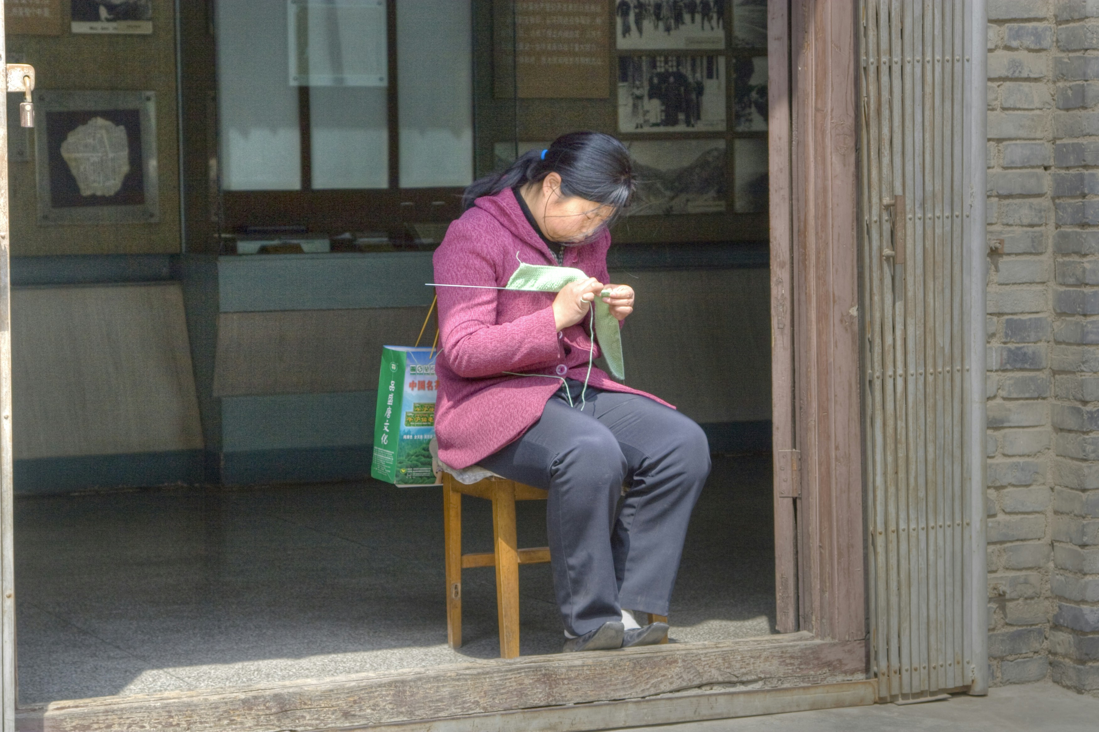Woman knitting in doorway somewhere in China