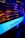 An illuminated blue strip with the word 'ELEKTRA' written on it, likely part of a machine or device. The surrounding area is dark with reflections of warm orange and purple hues on metallic ridges.