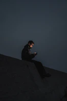 man in black jacket sitting on the edge of a building