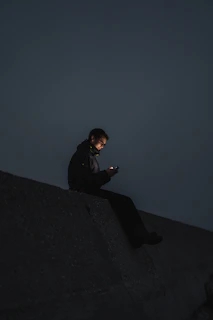 man in black jacket sitting on the edge of a building