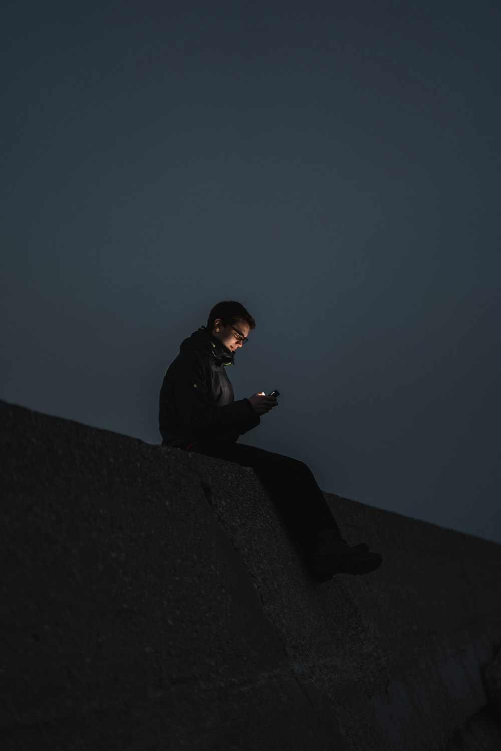 homem em jaqueta preta sentado na borda de um edifício