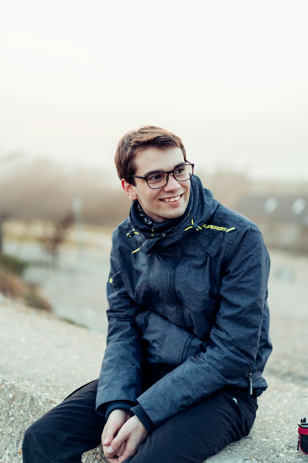 man in black jacket and blue denim jeans sitting on ground during daytime