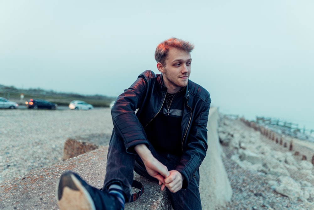 man in black jacket sitting on rock during daytime