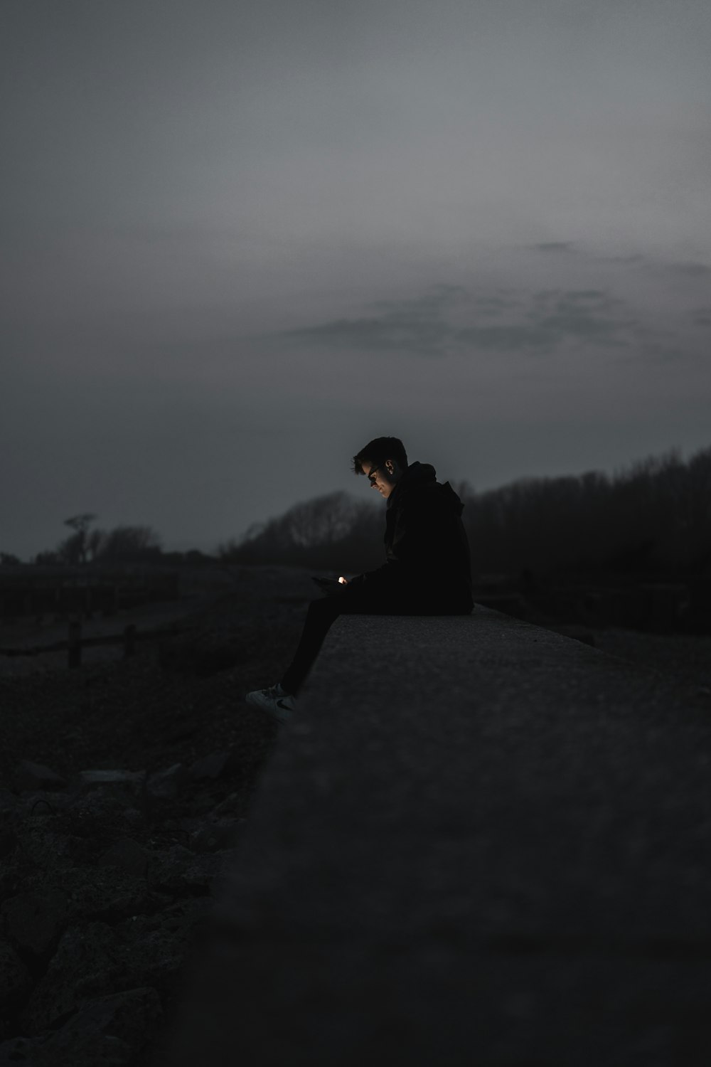 man in black jacket sitting on gray concrete pavement during daytime