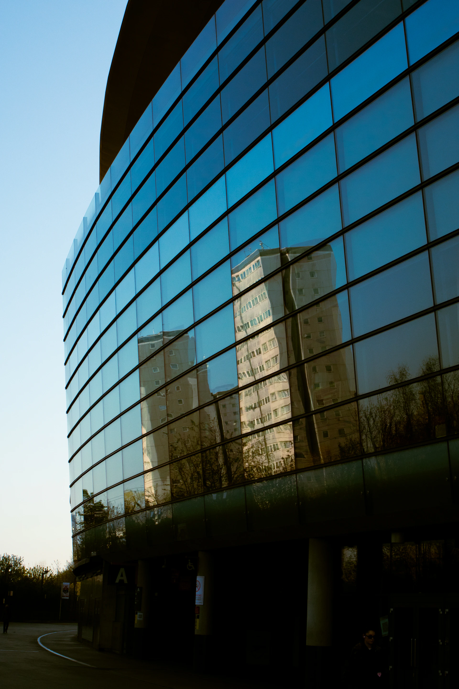 A sleek modern residential building with large glass windows reflecting the surrounding trees under a clear blue sky.