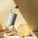 A stylish water bottle with a bamboo cap is placed next to a piece of ginger, a pineapple slice, and a lime slice, all on a light-colored surface. The scene is well-lit with shadows, creating a fresh and healthy vibe.