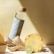 A stylish water bottle with a bamboo cap is placed next to a piece of ginger, a pineapple slice, and a lime slice, all on a light-colored surface. The scene is well-lit with shadows, creating a fresh and healthy vibe.