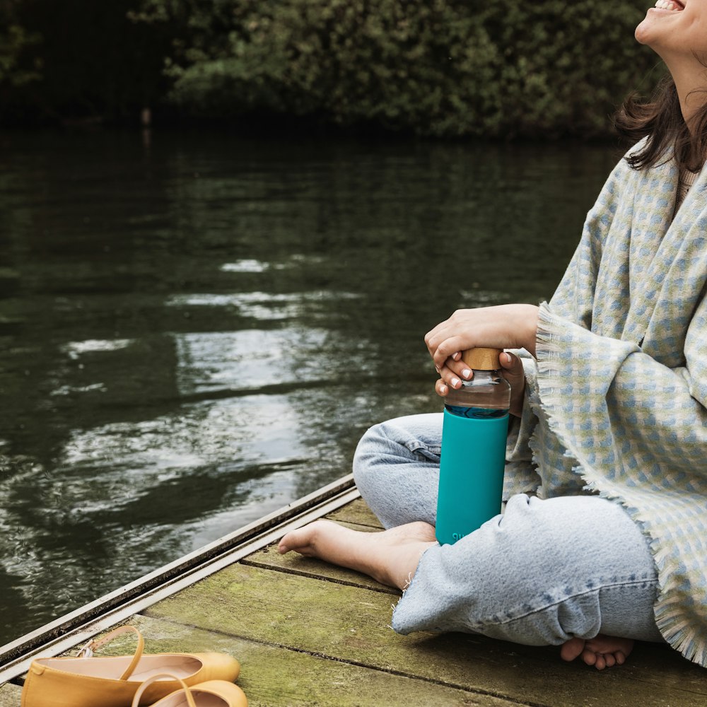 woman in gray sweater and gray pants sitting on brown wooden boat on river during daytime