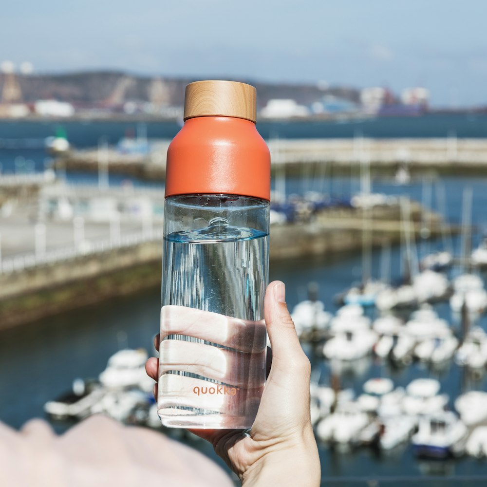 Persona sosteniendo una botella de vidrio naranja y transparente