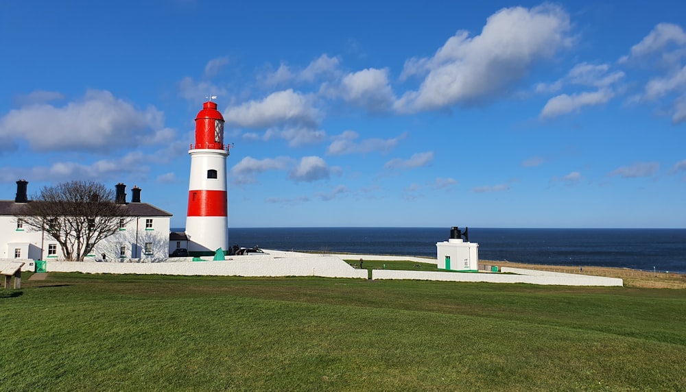 weißer und roter Leuchtturm in der Nähe von Gewässern unter blauem Himmel tagsüber