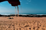 A hand holding a sand can with a backdrop of crashing ocean waves.
