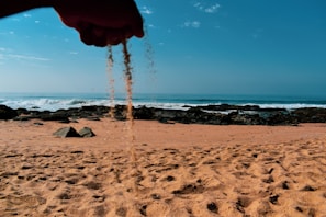 A hand holding a sand can with a backdrop of crashing ocean waves.