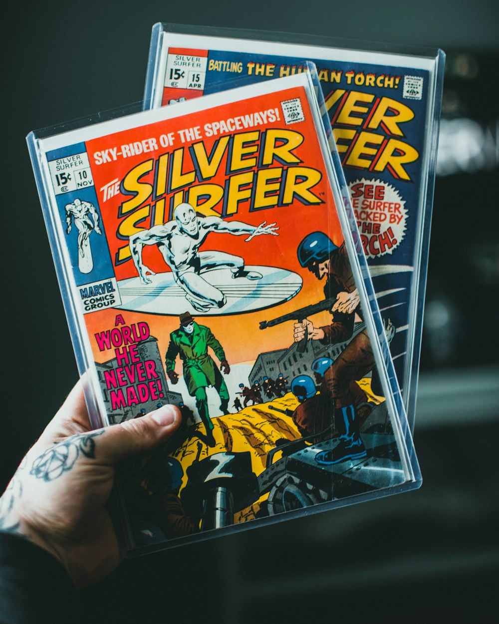 a person holding up two silver surfer comics