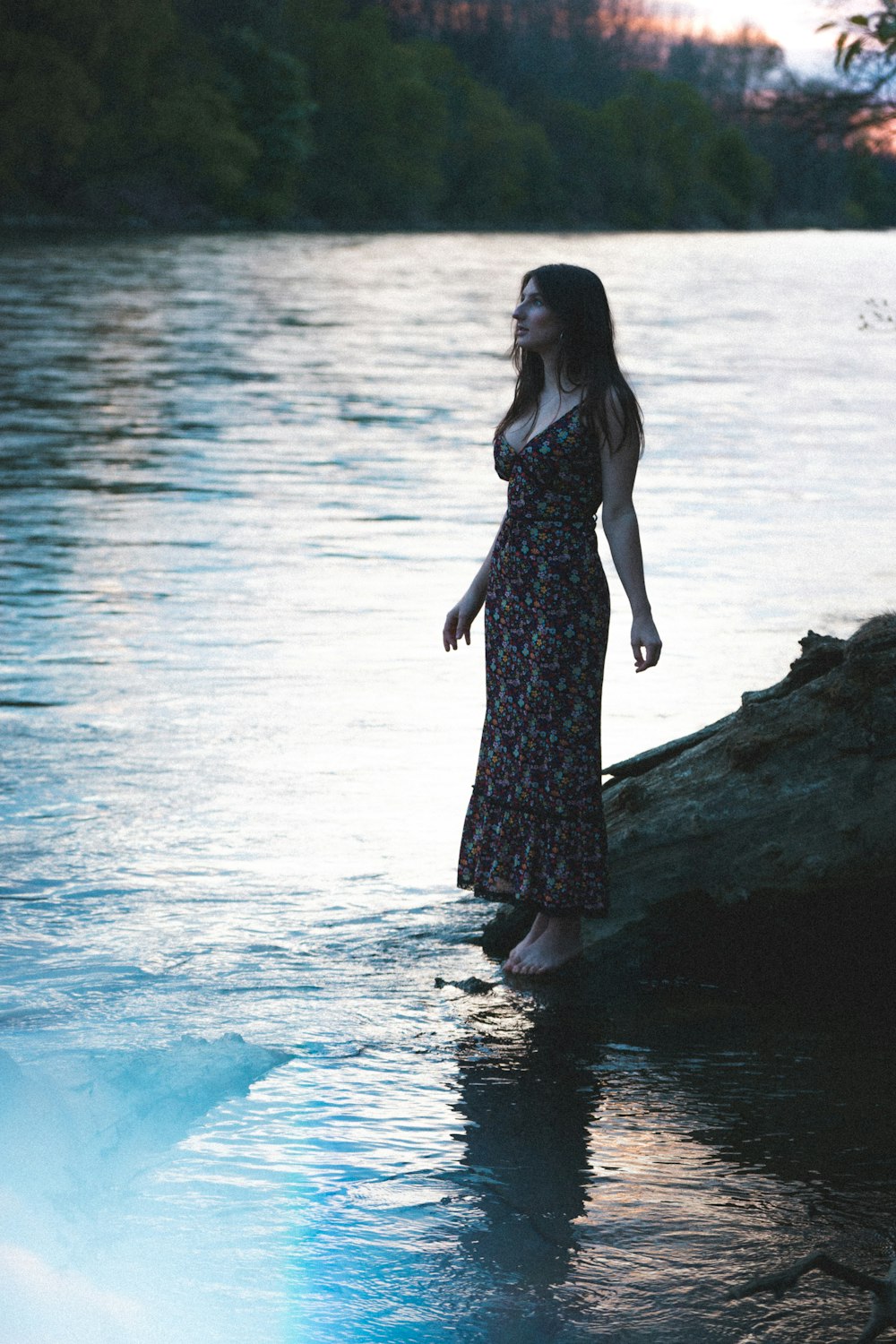 Frau in schwarzem Kleid, die tagsüber auf einem Felsen in der Nähe eines Gewässers steht