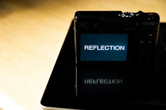 A modern digital camera with a bright lens reflecting a sunny outdoor scene.