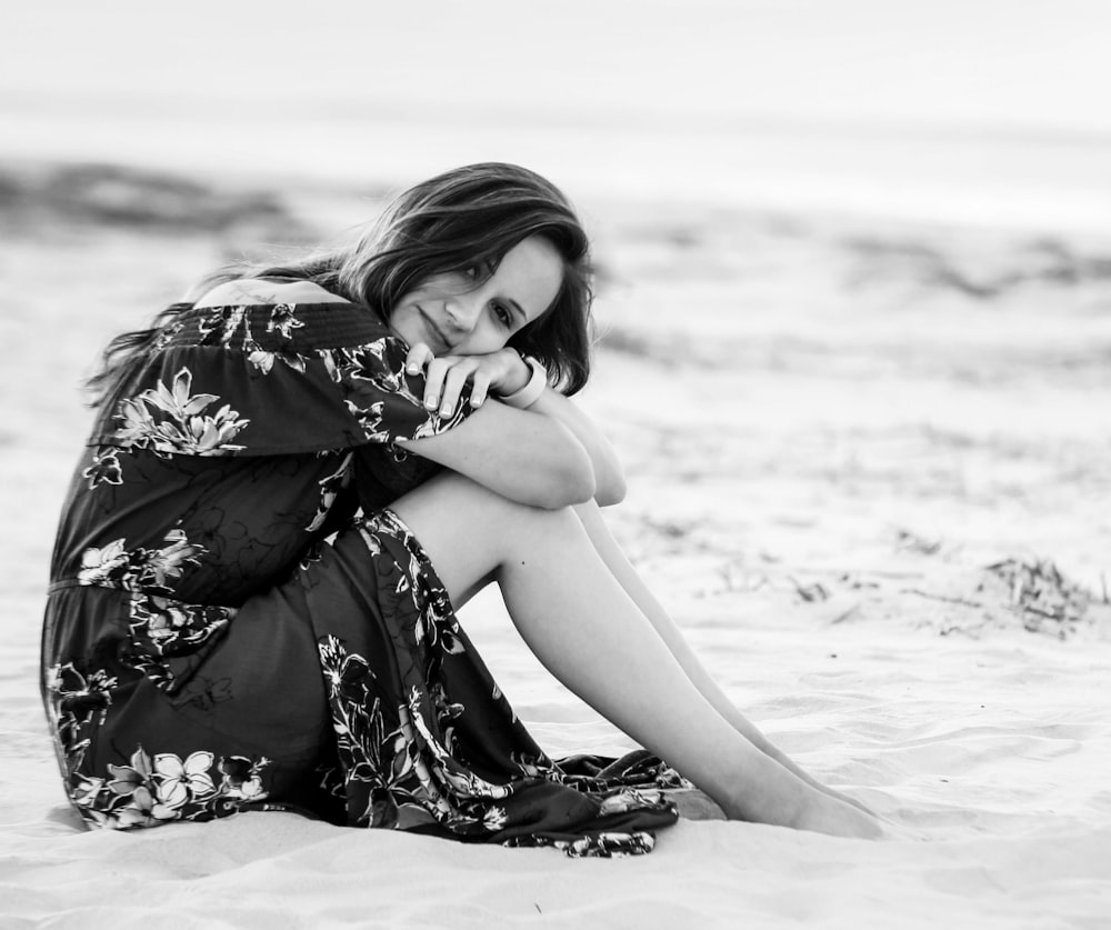 Frau in schwarz-weißem Blumenkleid sitzt am Strand