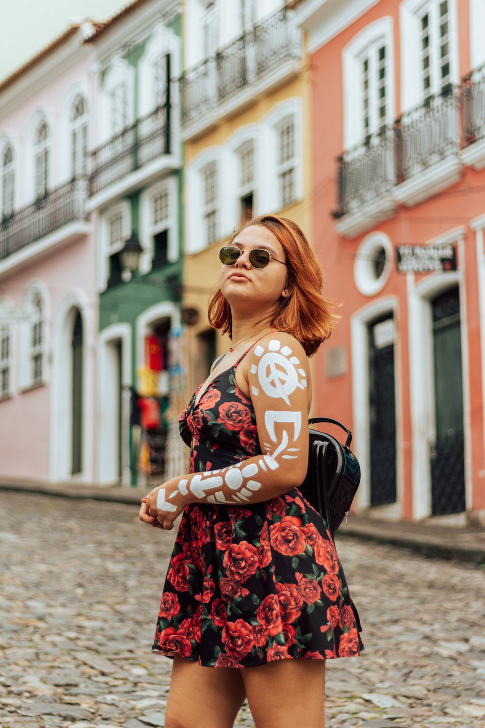 mulher no vestido floral preto e vermelho vestindo óculos de sol pretos em pé na rua durante o dia