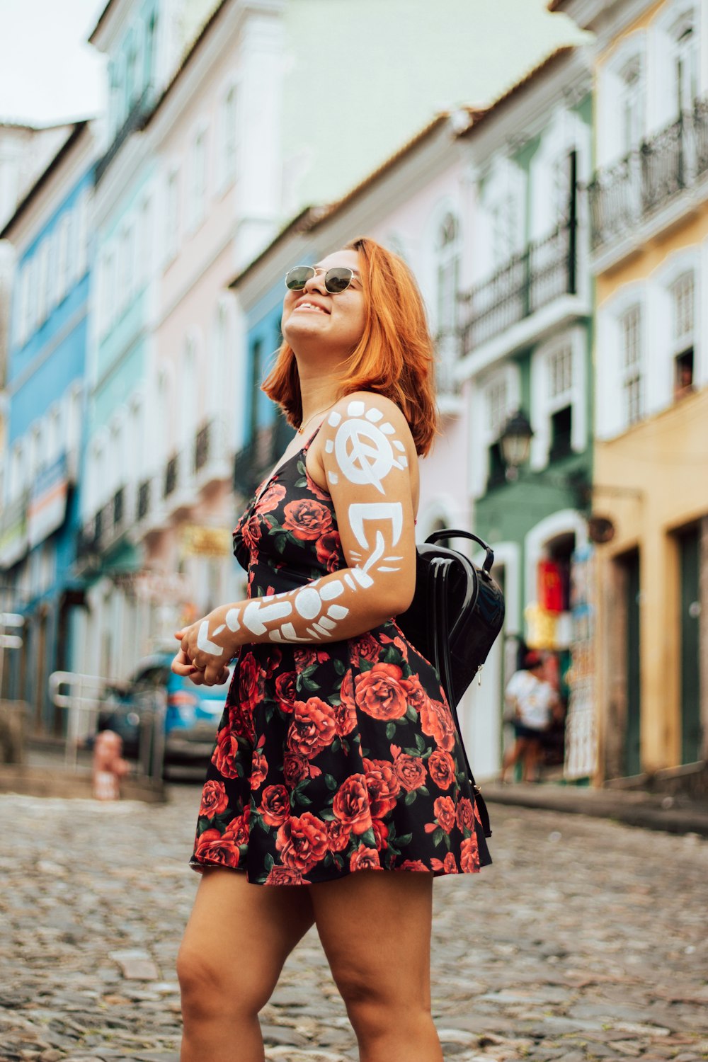 Mujer en vestido floral negro y rojo con gafas de sol negras de pie en la acera durante el día