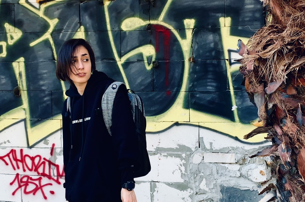 Femme en veste noire debout à côté d’un mur de graffitis