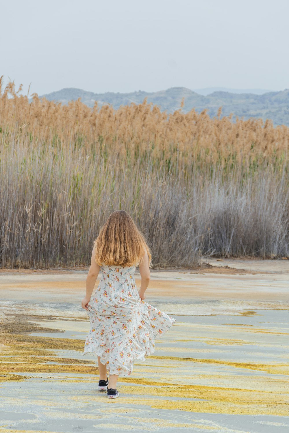 woman in white and red floral dress walking on brown sand during daytime