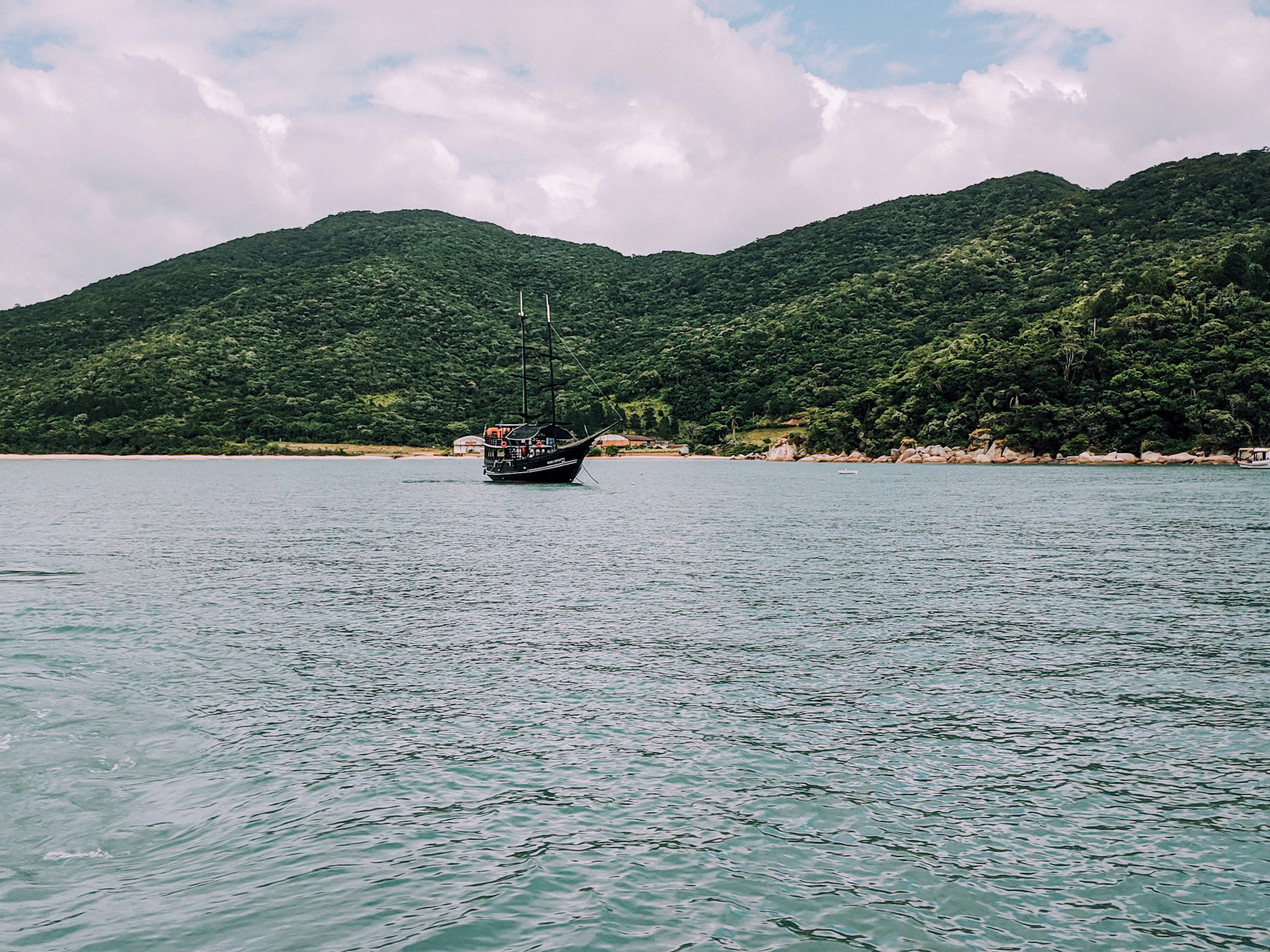 A breezy watercolor study of a sailboat drifting past lush green hills under a clear blue sky, evoking the peaceful spirit of island travel.