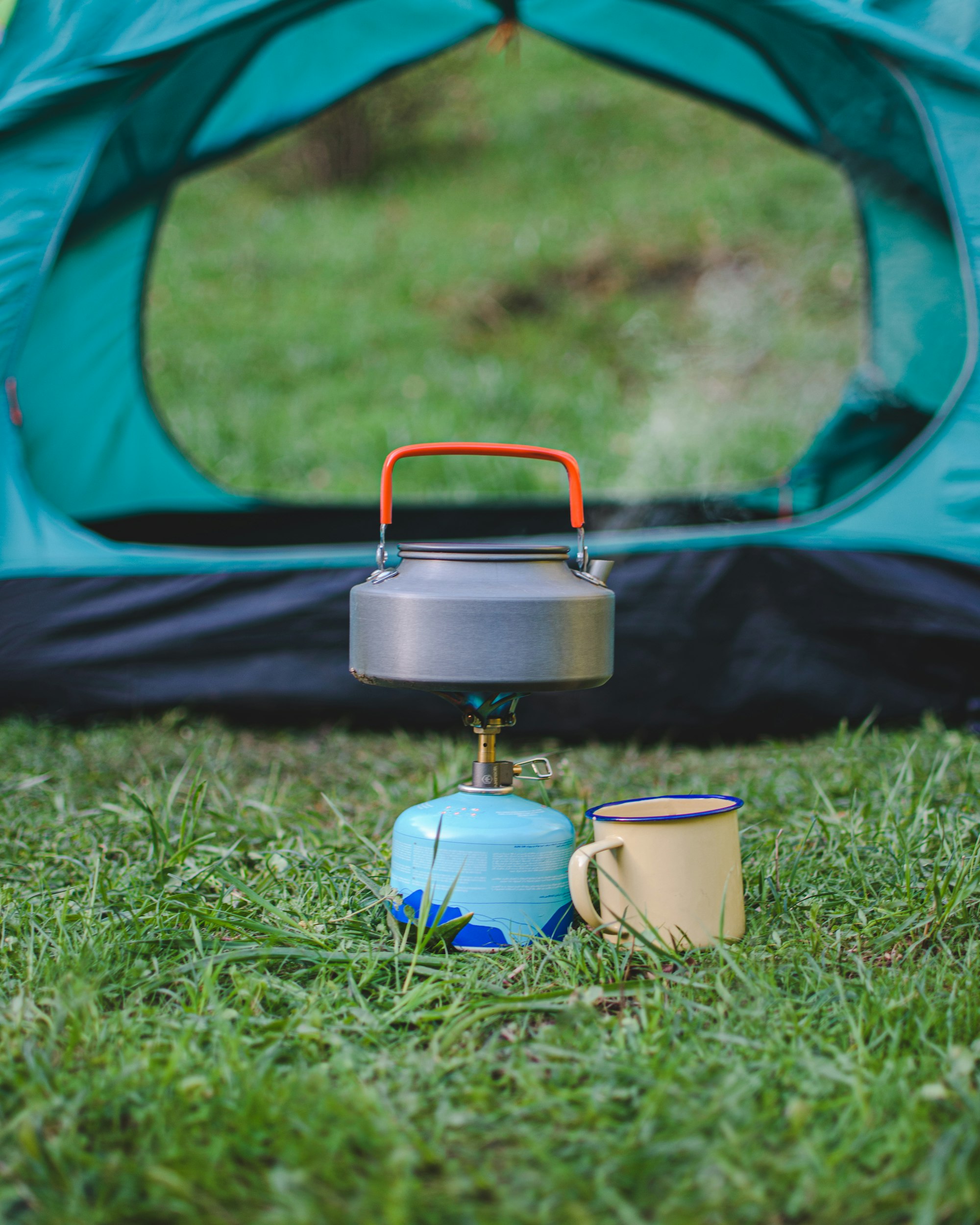 boiling water next to the travel mug in front of the camping tent.
