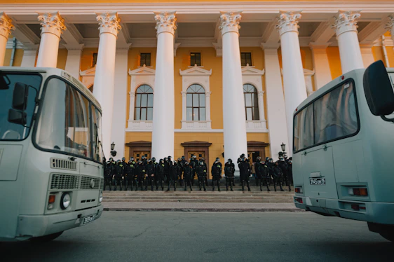 A professional security team in deep crimson uniforms standing confidently in front of a modern office building.