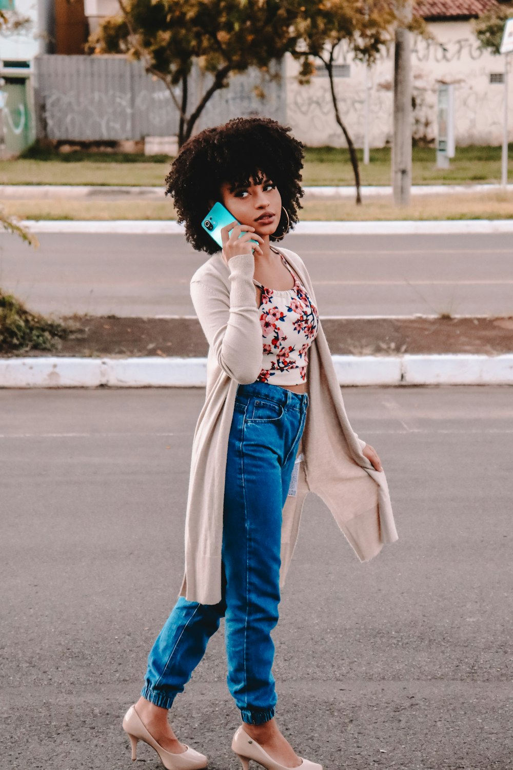woman in white and red floral long sleeve shirt and blue denim jeans standing on sidewalk