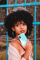 woman in white tank top holding blue smartphone