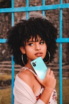 woman in white tank top holding blue smartphone